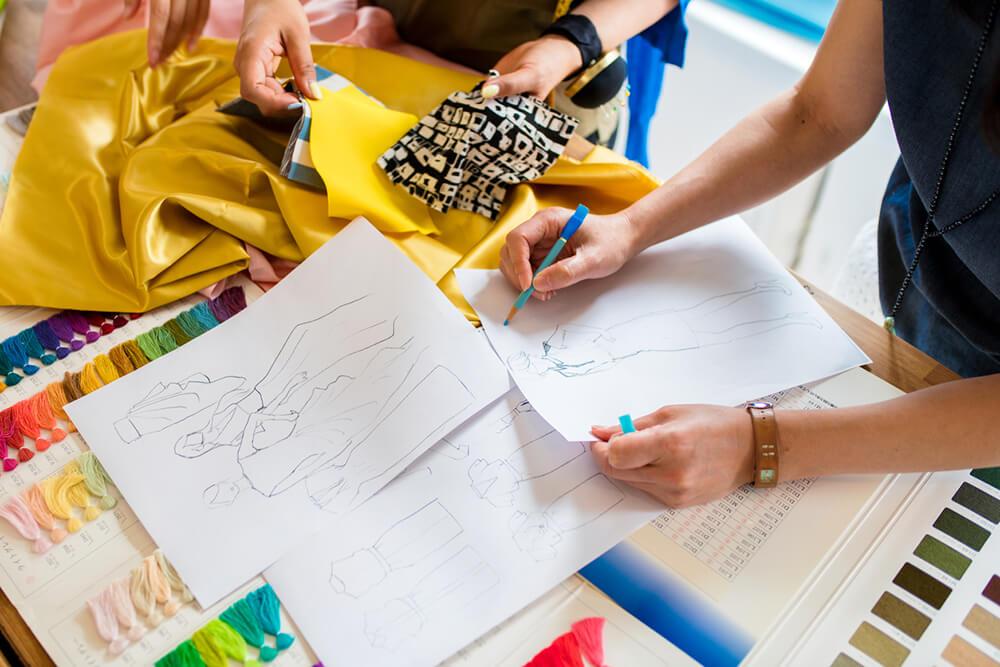 duas pessoas avaliando desenho de moda, tecidos e linhas para costura
